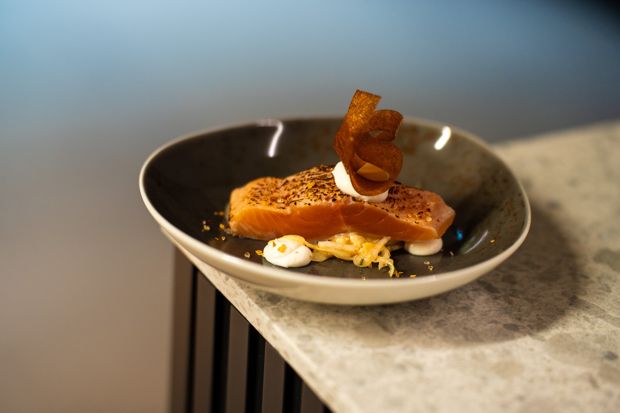 Ein Gourmet-Lachsfilet auf knackigem Gemüse, elegant angerichtet auf grauer Keramik - gefertigt mit dem Präzisionskochgeschirr von Fissler.