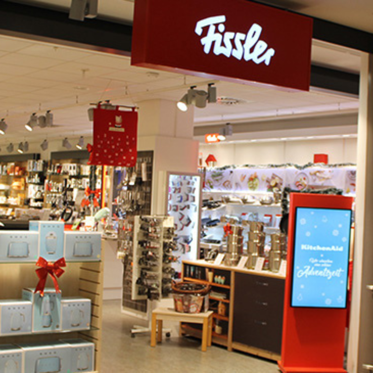 Eingang zum Fissler-Laden mit hochwertigen Töpfen, Pfannen und Kochgeschirr aus deutscher Produktion. Ein rotes Fissler-Schild und Geschenkboxen laden Sie ein.