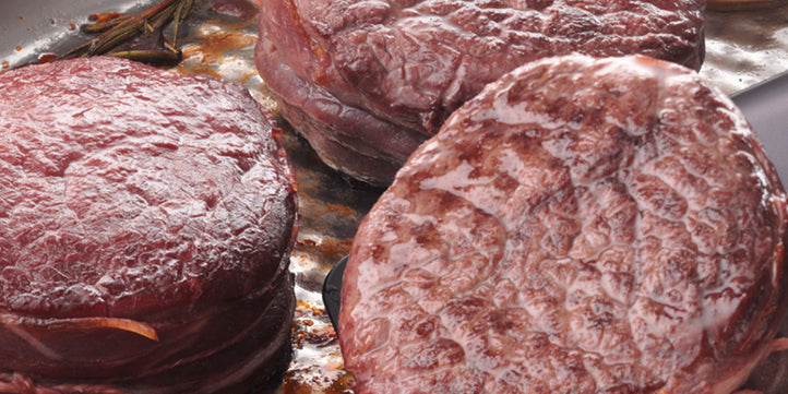 Drei dicke Stücke rohes rotes Fleisch beginnen in einer hochwertigen Fissler-Edelstahlpfanne zu braten, der Saft glänzt auf der Oberfläche.