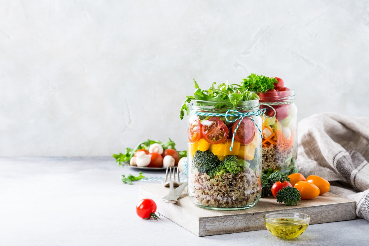 Zwei Gläser mit bunt geschichtetem Salat auf einem Holzbrett, daneben eine Schüssel mit Dressing - frische Zubereitung leicht gemacht mit der Präzision von Fissler.