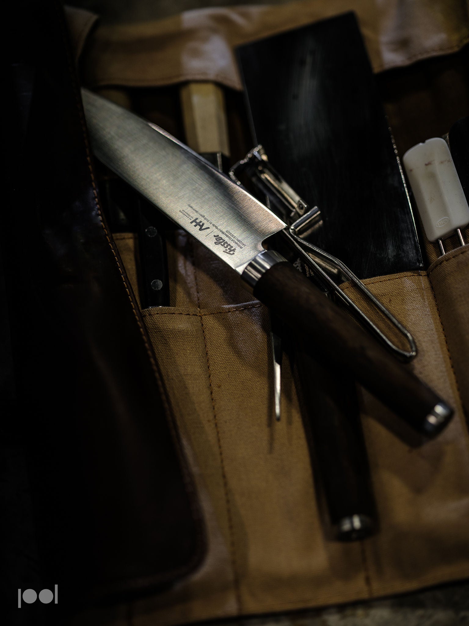 Ein präzise gefertigtes Fissler-Kochmesser mit dunklem Griff wird elegant auf einer hellbraunen Messerrolle präsentiert, ergänzt durch hochwertige Küchenwerkzeuge und -utensilien, die deutsche Qualität und zeitloses Design widerspiegeln.